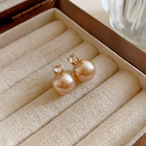 Macro view of elegant champagne pearl stud earrings with zircon inlay in a wooden box