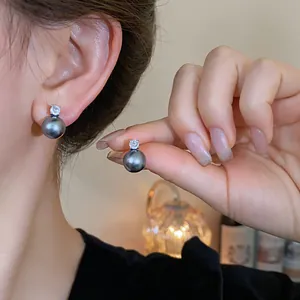 Close-up detail showing dark iridescent pearl stud earrings with a cubic zirconia top