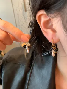 Detailed close-up of stylish peanut-shaped pendant earrings with black glass beads worn on ear