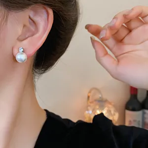 Close-up detail of elegant zircon pearl stud earrings worn by a model in soft ambient light