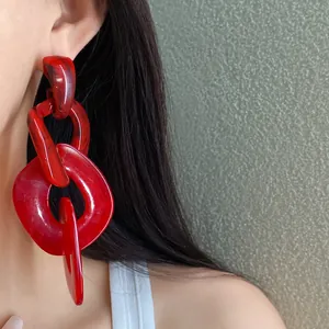 Close-up detail of oversized red acrylic irregular chain drop earrings worn by a female model