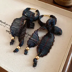 Detailed view of vintage plaid fabric bow earrings with fringe and gold bead accents