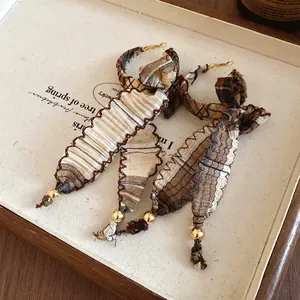 Close-up of retro ethnic plaid fabric bow earrings with gold bead tassels on a tray