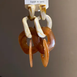 Close-up of acrylic irregular chain earrings featuring cream and amber marble texture