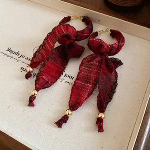 Detailed macro view of red plaid fabric bow tassel earrings with gold accents on a display.