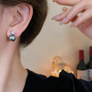 Close-up view of elegant dark gray pearl and sparkling zircon stud earrings worn on ear