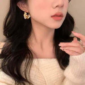 Elegant floral pearl and crystal stud earrings with silver needles worn by a model