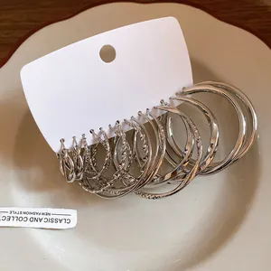 Detailed view of multiple silver geometric twisted hoop earrings arranged on white display card