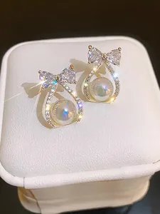 Macro detail of elegant mermaid pearl earrings featuring a crystal-encrusted gold bow design