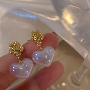 Macro view of elegant gold rose stud earrings with iridescent heart-shaped mermaid pearls.