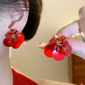Close-up of vintage red floral shell earrings worn on ear and held by fingers