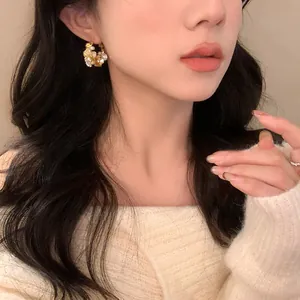 Detailed view of an Asian model wearing elegant gold-toned flower and pearl stud earrings