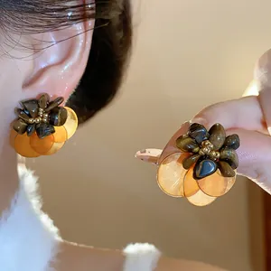 Detailed macro view of vintage shell and tiger eye stone floral earrings shown on ear and hand