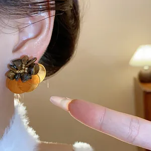 Detailed close-up of vintage tiger's eye stud earrings with golden shell petals on ear.