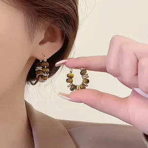 Retro gold-plated hoop earrings with natural tiger's eye beads shown on ear and hand.