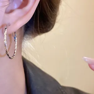 Detailed close-up showing a large silver twisted geometric hoop earring worn on an ear