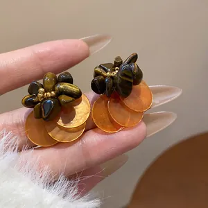 Close-up of vintage ethnic tiger eye and shell disc stud earrings with gold accents.