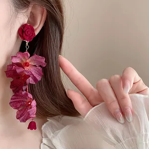 Elegant red velvet rose and layered fabric flower drop earrings shown on model's ear.