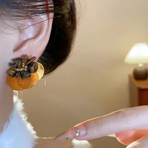 Close-up detail of vintage tiger eye stone stud earrings with gold shell petals on a model.