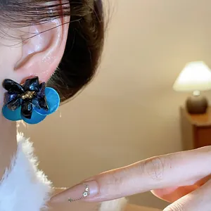 Close-up of retro floral stud earrings featuring black tiger eye and blue shell petals.