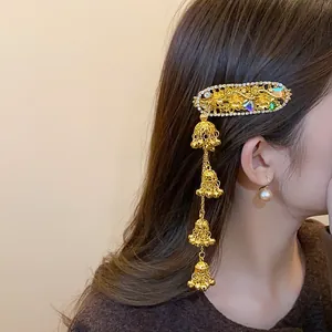 Detail view of ethnic gold hair clip with rhinestones and long bell tassels on hair.