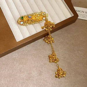 Close-up of elegant gold-tone hair clip with intricate floral engraving and bell tassels.