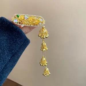 Detailed view of an ornate golden hair clip featuring rhinestone oval flowers and bell tassels