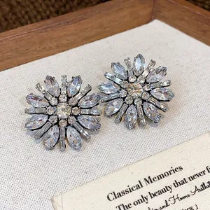 Primo piano di eleganti orecchini a fiore con strass in un vassoio di legno rustico.