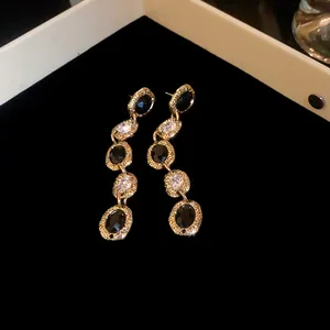 Macro detail of elegant gold drop earrings featuring black stones and clear crystals.