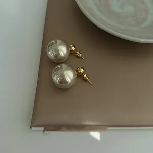 Detailed view of elegant pearl and gold bead stud earrings presented on a textured brown surface.