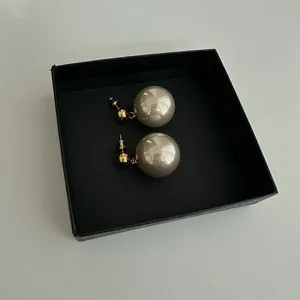 Detailed macro view of champagne pearl stud earrings with gold plating inside a black jewelry box