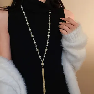 Close-up view of long faux pearl tassel necklace layered over a black turtleneck top.