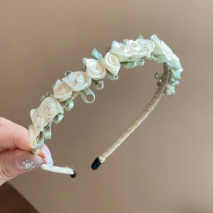 Nahaufnahme von cremefarbenen Satinrosen und grünen Blättern auf einem eleganten Haarreif