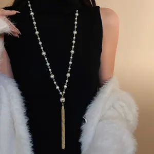 Elegant long faux pearl tassel necklace layered over a black winter sweater for chic look