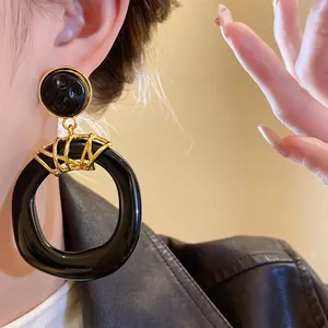 Primo piano di eleganti orecchini pendenti vintage in resina nera irregolare con dettagli oro.
