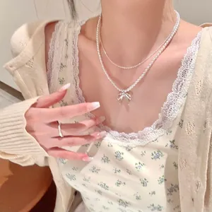 Detailed view of elegant pearl necklace with silver bow pendant worn with floral camisole
