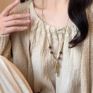 Détail d'un collier vintage de style ethnique avec perles en bois et glands métalliques.