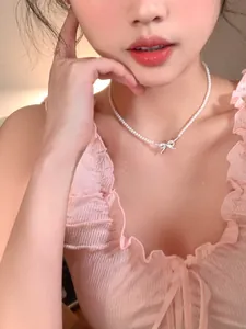 Close-up of dainty zircon bow pendant on a delicate pearl necklace worn by a model.