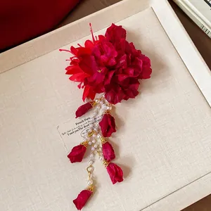 Macro view of a deep red fabric flower hair clip featuring elegant pearl tassels and rosebuds