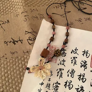 Gros plan d'un collier zen en perles de bois avec pendentif fleur en paille tressée.