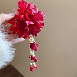 Macro view of a red fabric flower hair clip featuring elegant pearl tassels and rosebuds.