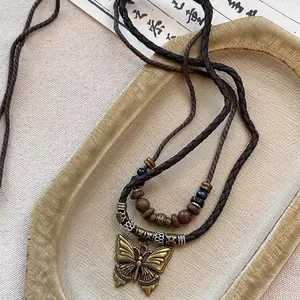 Gros plan d'un pendentif papillon en bronze vintage avec des perles en bois texturées.