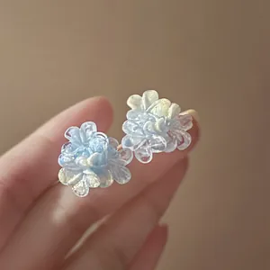 Close-up of delicate blue resin flower stud earrings with a pearlescent gradient finish.