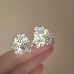 Macro detail of iridescent resin flower stud earrings held on fingertips for scale