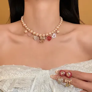 Detail view of heart and bow charms on a pink pearl necklace and earrings jewelry set.