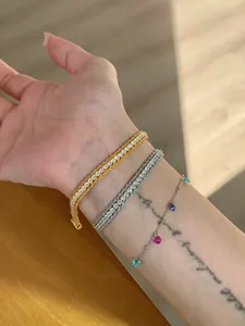 Close-up of stacked gold and silver zircon bracelets with colorful stone charms