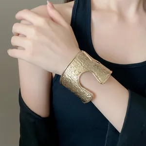 Bracciale rigido dorato minimalista con texture increspata e dettaglio traforato a forma di U