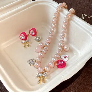 Detailed view of pink pearl necklace and heart bow earrings set with sparkling rhinestones