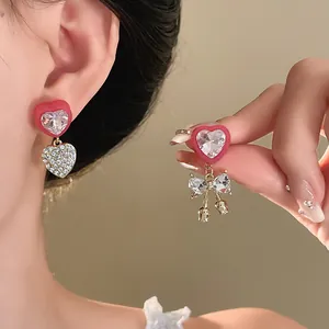 Detailed macro view of asymmetric red heart earrings with sparkly bow and rhinestone dangles.