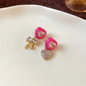 Macro detail of asymmetric pink heart earrings with rhinestone bow and heart charms.